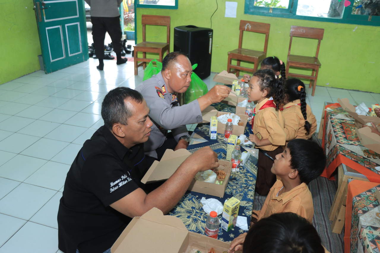 Kasi Humas Iptu Samsul Anwar SH menyuapi salah satu siswa SDN 6 Penataran. SP/Lestariono