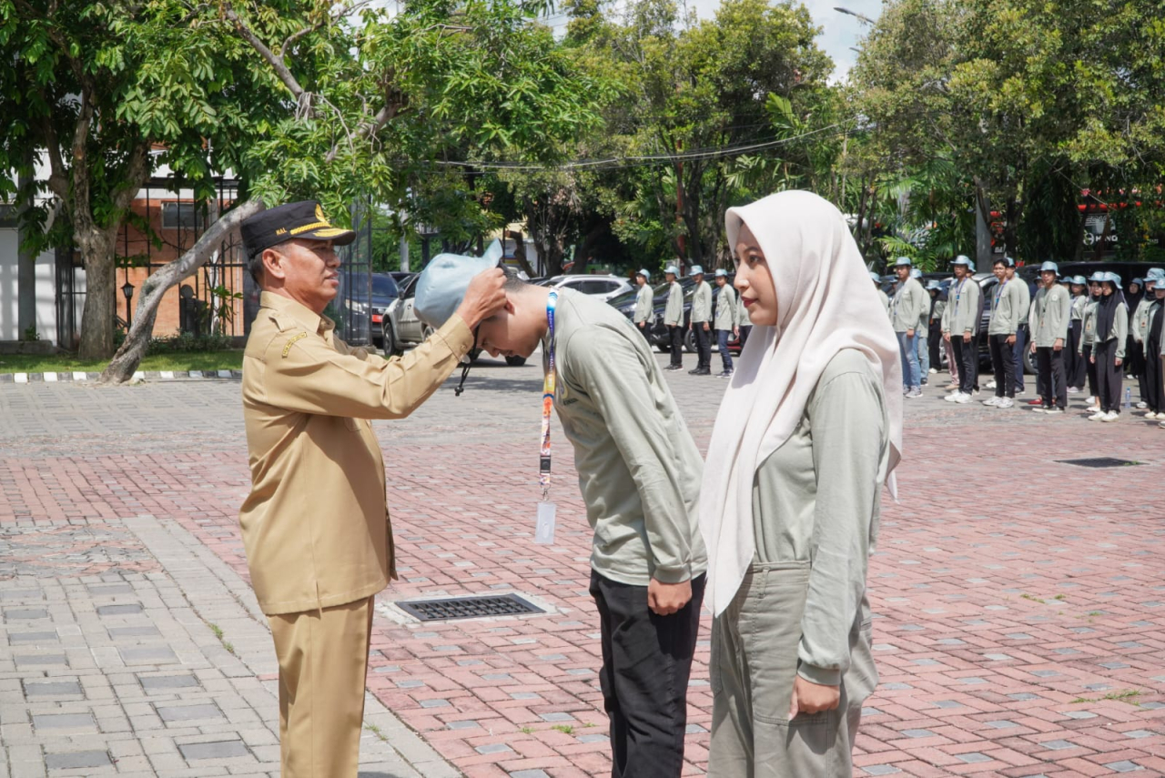 Sekda Lamongan Moh. Nalikan mengalungkan tanda pengenal kepada mahasiswa yang akan melaksanakan BBK. SP/IST