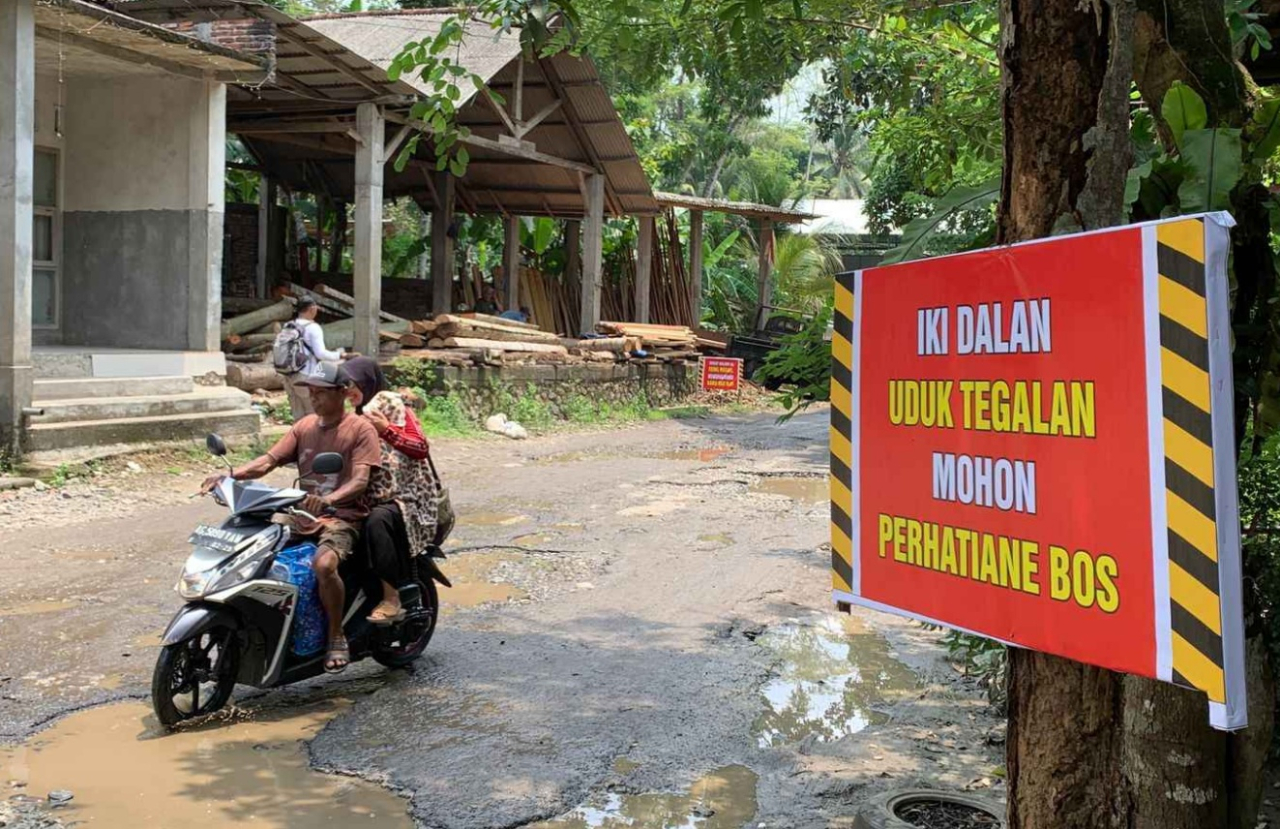 Salah seorang warga melintasi jalan di Kabupaten Trenggalek yang rusak dan tergenang air hujan. SP/ TRG