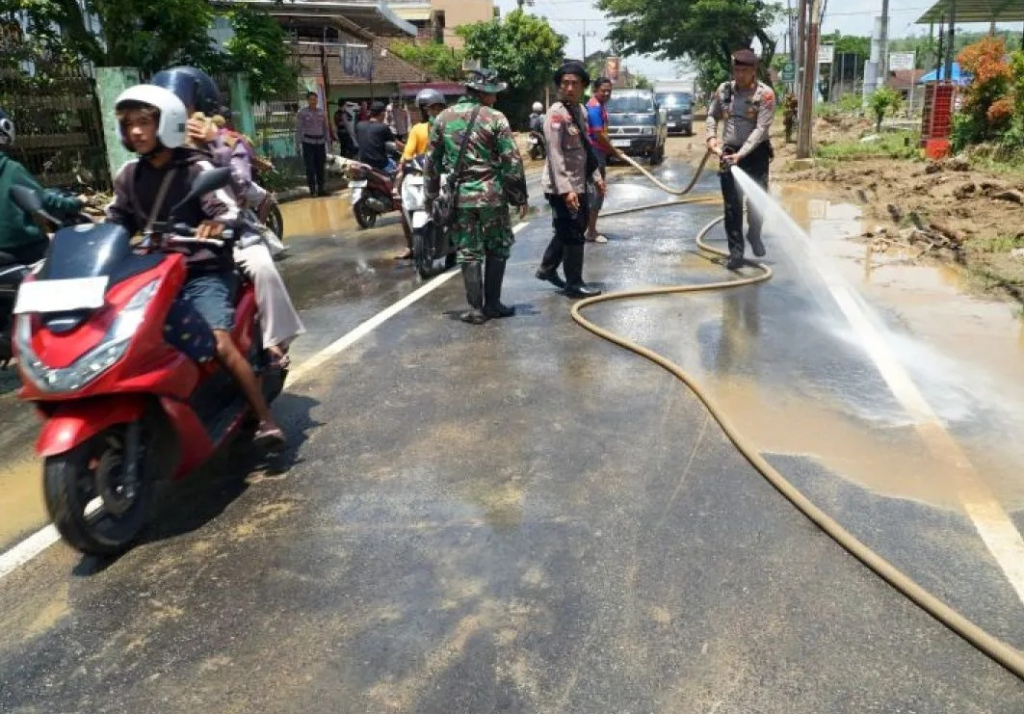 Petugas menyemprotkan air untuk membersihkan lumpur yang menutup akses Jalan Raya Popoh, Tulungagung, Jawa Timur. SP/ TLG