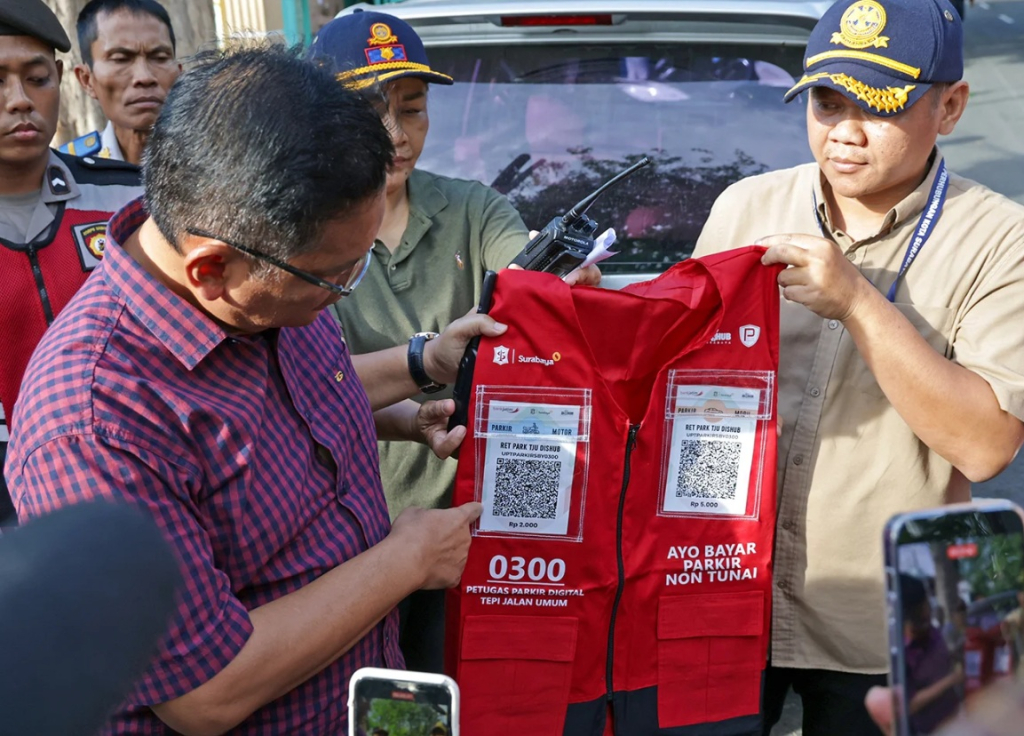 Plt Kepala Dinas Perhubungan Kota Surabaya Trio Wahyu Bowo menunjukkan rompi resmi juru parkir digital yang dilengkapi kode QRIS saat sosialisasi sistem parkir non-tunai di Surabaya. SP/ SBY