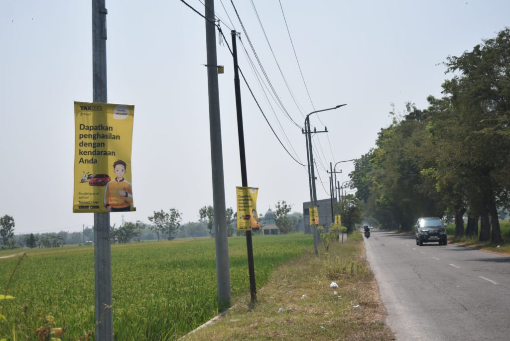 Spanduk yang terpasang di fasilitas penerangan jalan di sepanjang jalan Ahmad Yani, Area sawah/kebun Kaibon Kecamatan Geger Kabupaten Madiun.