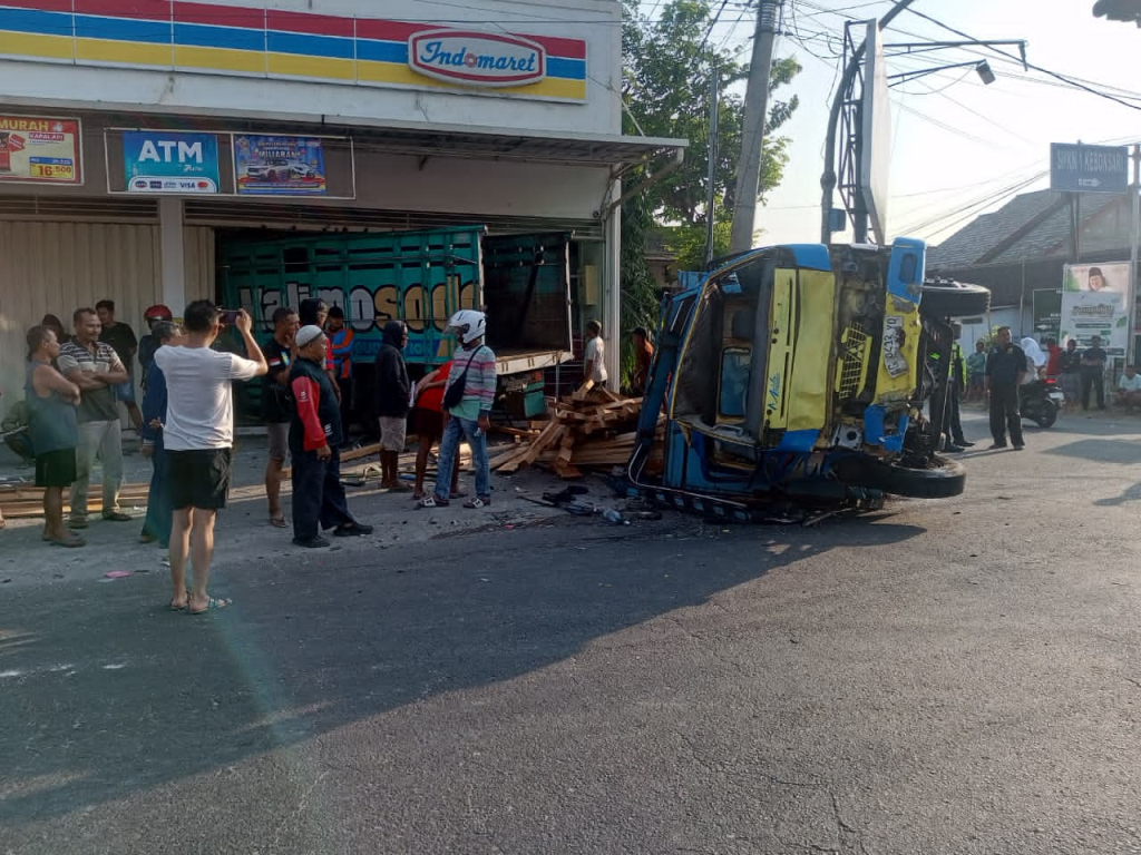 Kecelakaan dua truk di Simpang Empat Ngujur Kabupaten Madiun, Senin (7/9/2026). Salah satu truk bermuatan kayu tampak terguling di depan Indomaret setelah terlibat tabrakan dengan truk lainnya. SP/WAF