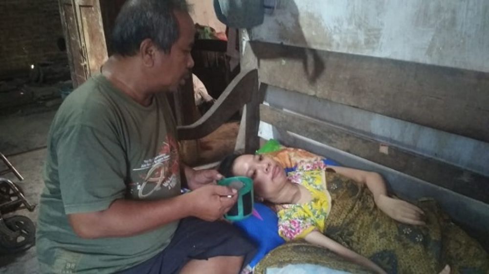 Kustomo saat menyuapi anaknya yang mengalami kelumpuhan total. (SP/M. Yusuf) 