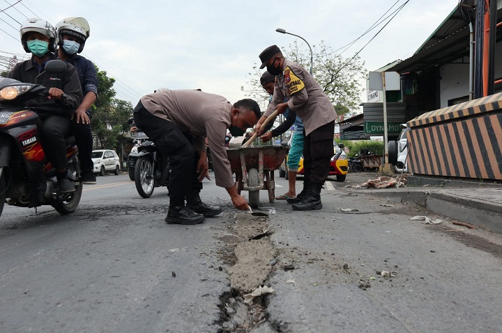Anggota Polsek Manyar saat menambal jalan berlubang di atas jembatan Desa Sukomulyo, Kecamatan Manyar, Gresik. SP/Grs
