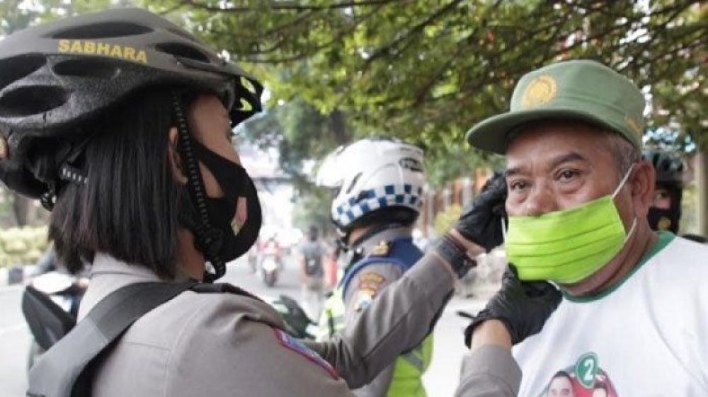 Salah seorang anggota polwan dari Polresta Malang Kota membagikan masker kepada masyarakat sekitar. 