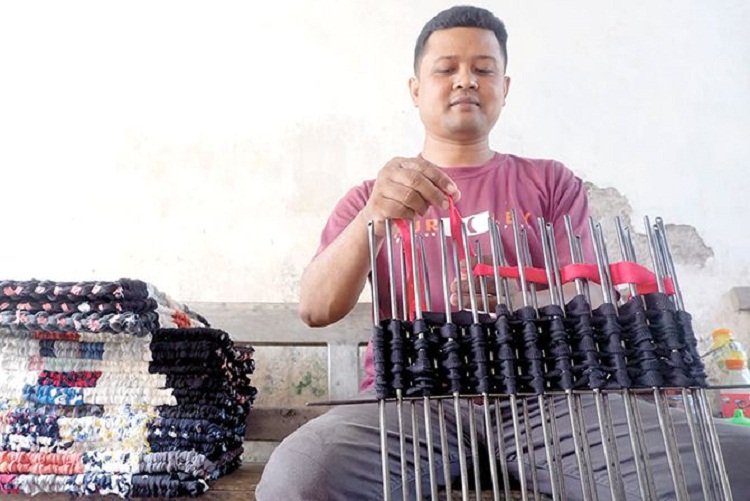 Hasanuddin sedang menganyam perca kain kaus untuk dibentuk menjadi sebuah keset rumahan. SP/ TLG