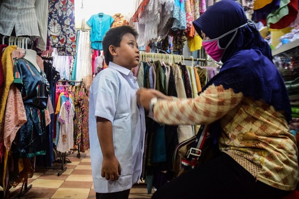 Terlihat, seorang ibu mengantarkan putranya, sedang mencoba seragam sekolah di Pasar Soponyono Rungkut, Surabaya, Minggu (12/7/2020), yang akan dipakai sekolah online hari pertama Senin hari ini.  SP/Patrik Cahyo