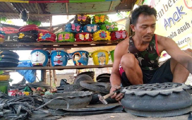 Ronald Kayon tengah memaku potongan ban bekas menjadi pot bunga di bengkel. SP/ MJK