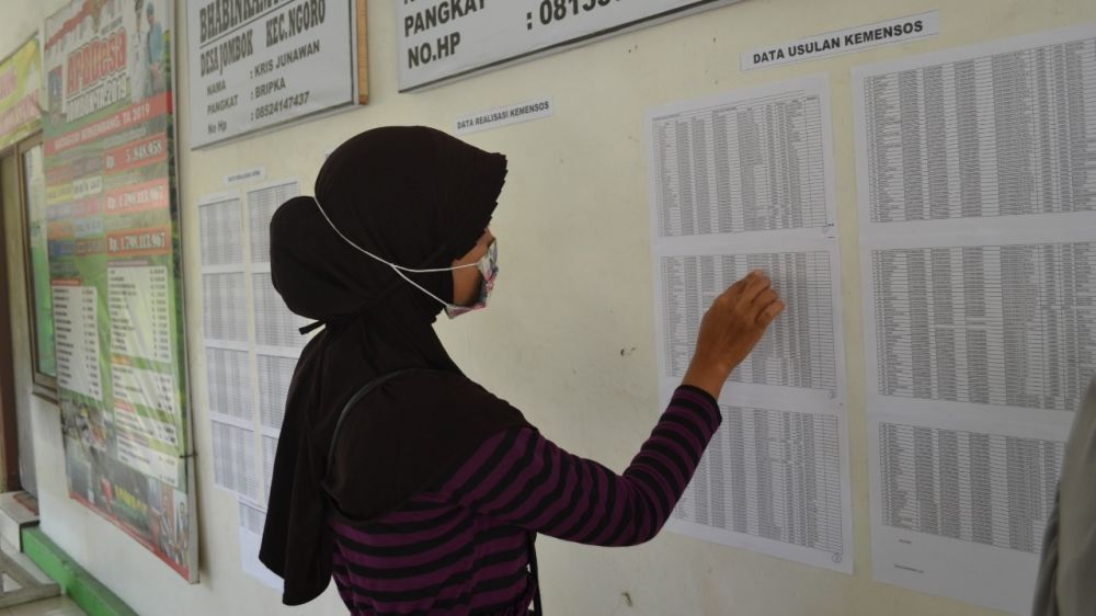 Warga saat melihat daftar penerima bansos Covid-19 yang tertempel di balai desa. (SP/M. Yusuf) 