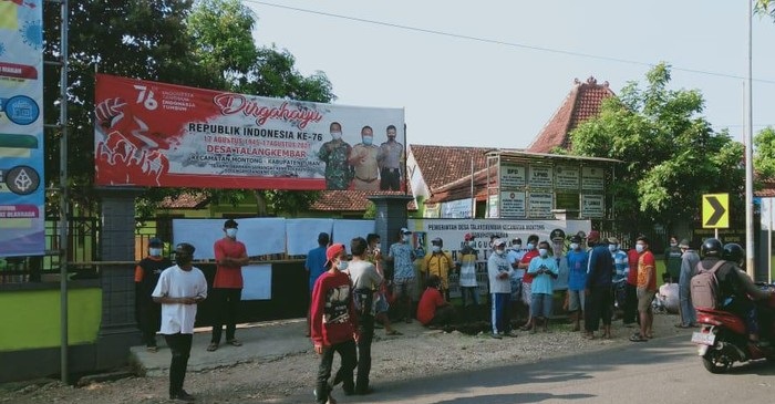 Warga bergerombol menduduki pintu gerbang balai desa.