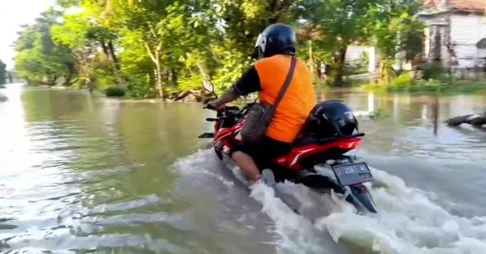 Salah satu pemotor nekad menerobos genangan air akibat luapan sungai Bengawan Njero.