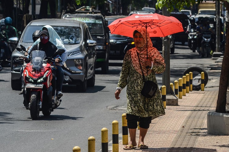 Terik matahari yang panas menyengat membuat warga khawatir hingga menggunakan payung dijalan. SP/ SBY