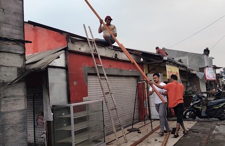 Warga memperbaiki atap toko yang rusak akibat diterjang angin puting beliung.