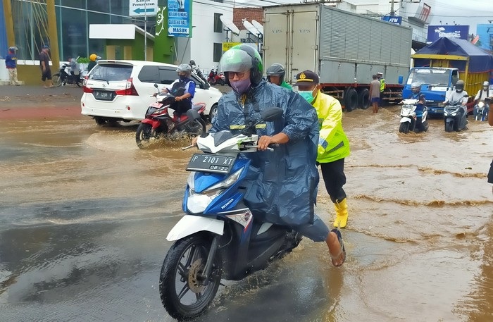 Tampak petugas kepolisian membantu mendorong sejumlah pengendara motor yang motornya mogok saat melintasi jalanan yang terendam air luapan sungai Bagong.